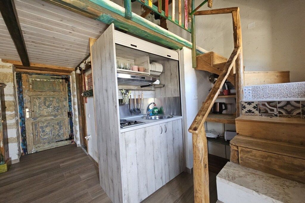Cocina compacta con encimera de madera, un lavabo y una escalera que sube a un nivel superior.