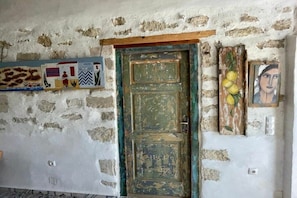Ein rustikaler Raum mit Steinwand, einer grünen Tür und verschiedenen Kunstwerken, darunter eine Giraffe, ein Schachbrett und ein Gemälde mit Zitronen.
