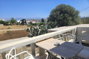 Eine Terrasse mit Tisch und Stühlen, die auf eine Landschaft mit Kakteen und in der Ferne Gebäuden blickt.