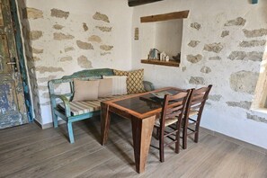 Ein rustikaler Raum mit einem Holztisch, Stühlen, einer Steinwand und einer Holzbänkchen mit Kissen.