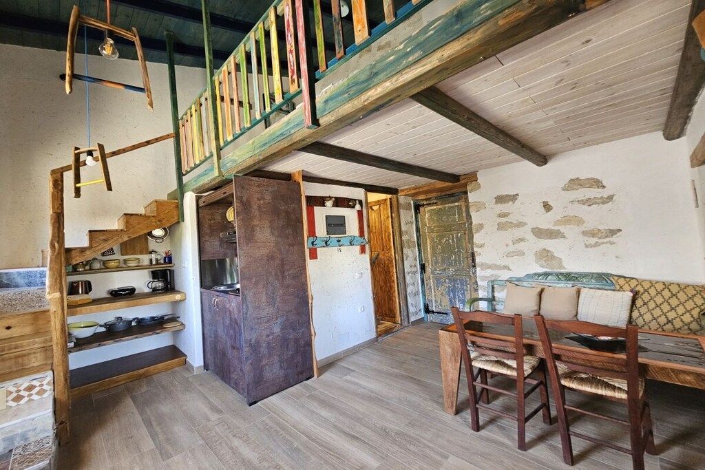 Un intérieur rustique avec un escalier en bois, un coin repas avec des chaises et un espace cuisine.