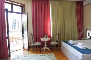 A hotel room with a bed, two chairs, a small table, and a window with curtains.