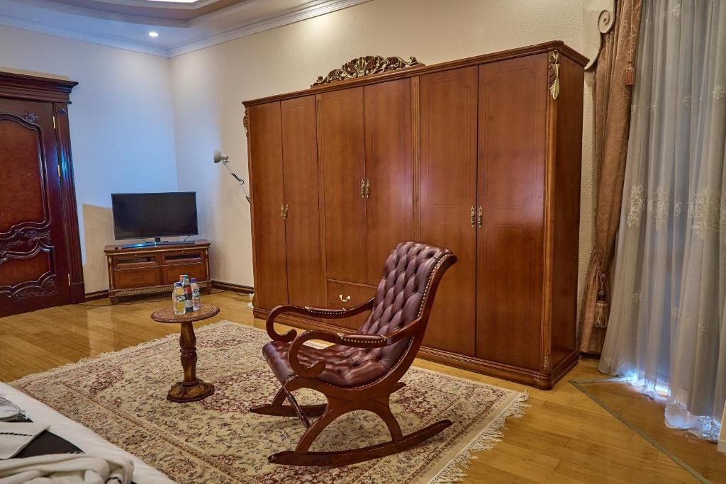Una sala de estar con un armario de madera, un sillón mecedor de cuero, una pequeña mesa redonda con botellas y un televisor sobre un mueble bajo.