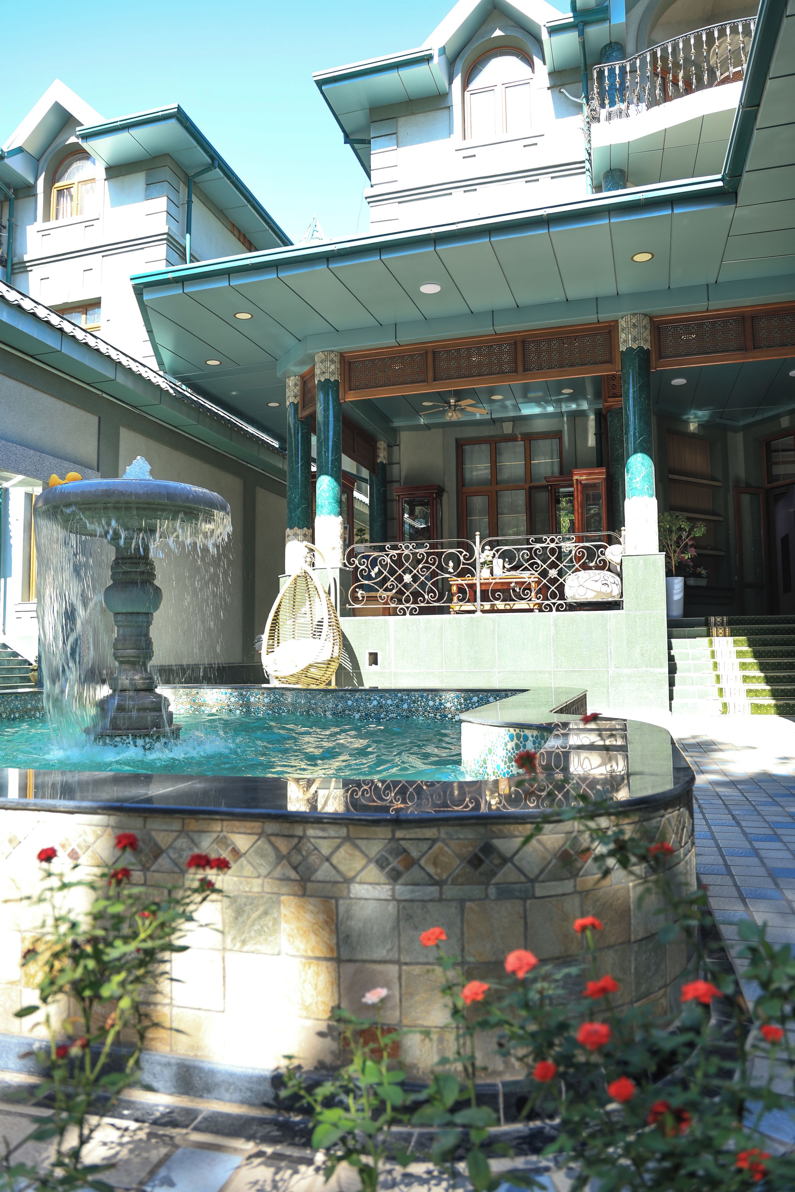 Un edificio con una fuente, un balcón con barandillas ornamentales y una zona de piscina con azulejos.