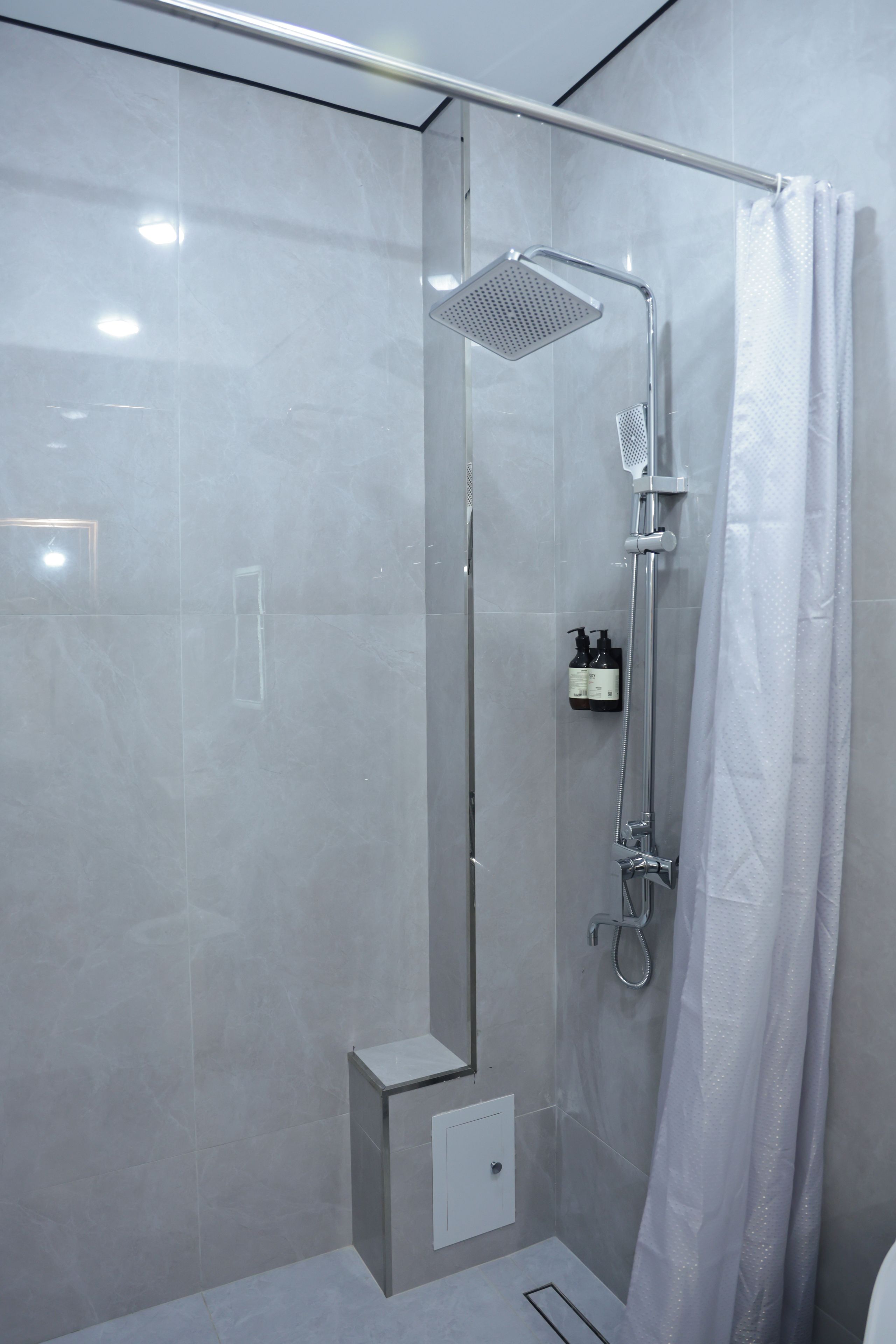 Box de chuveiro moderno com porta de vidro, chuveiro manual e painel de controle fixado na parede.