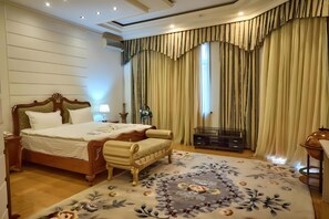 A hotel room with a large bed, a small sofa, a TV stand, and a decorative rug.