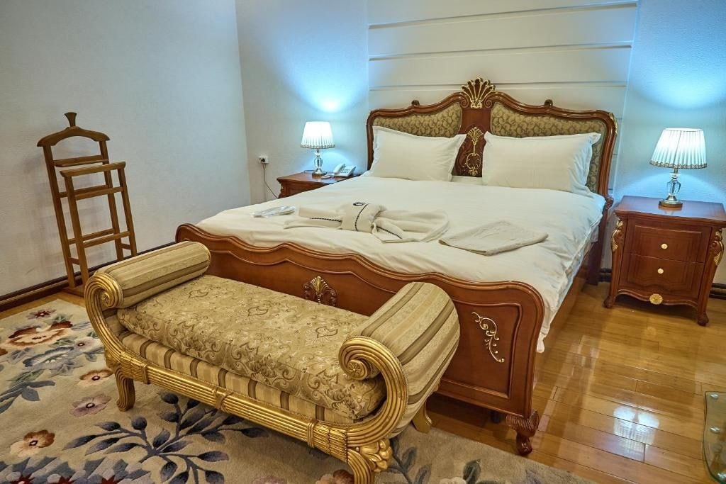 A bedroom with a large bed, bedside tables, a bench, and a floral-patterned rug.