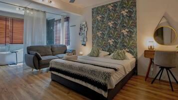 A modern bedroom with a large bed, a sofa, a desk, and a shower area.