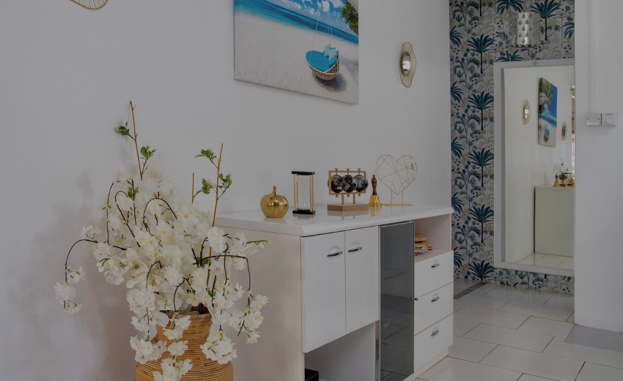 A bathroom with a white vanity, a mirror, and a wall with a tropical wallpaper.
