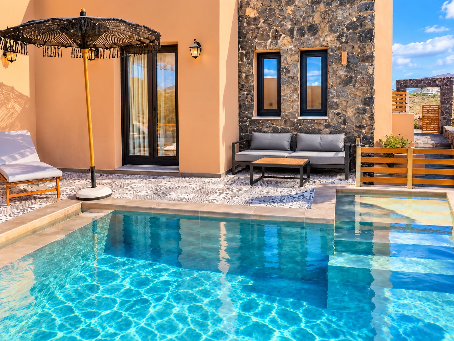 A pool area with a lounge chair, a table, and a stone wall with windows.
