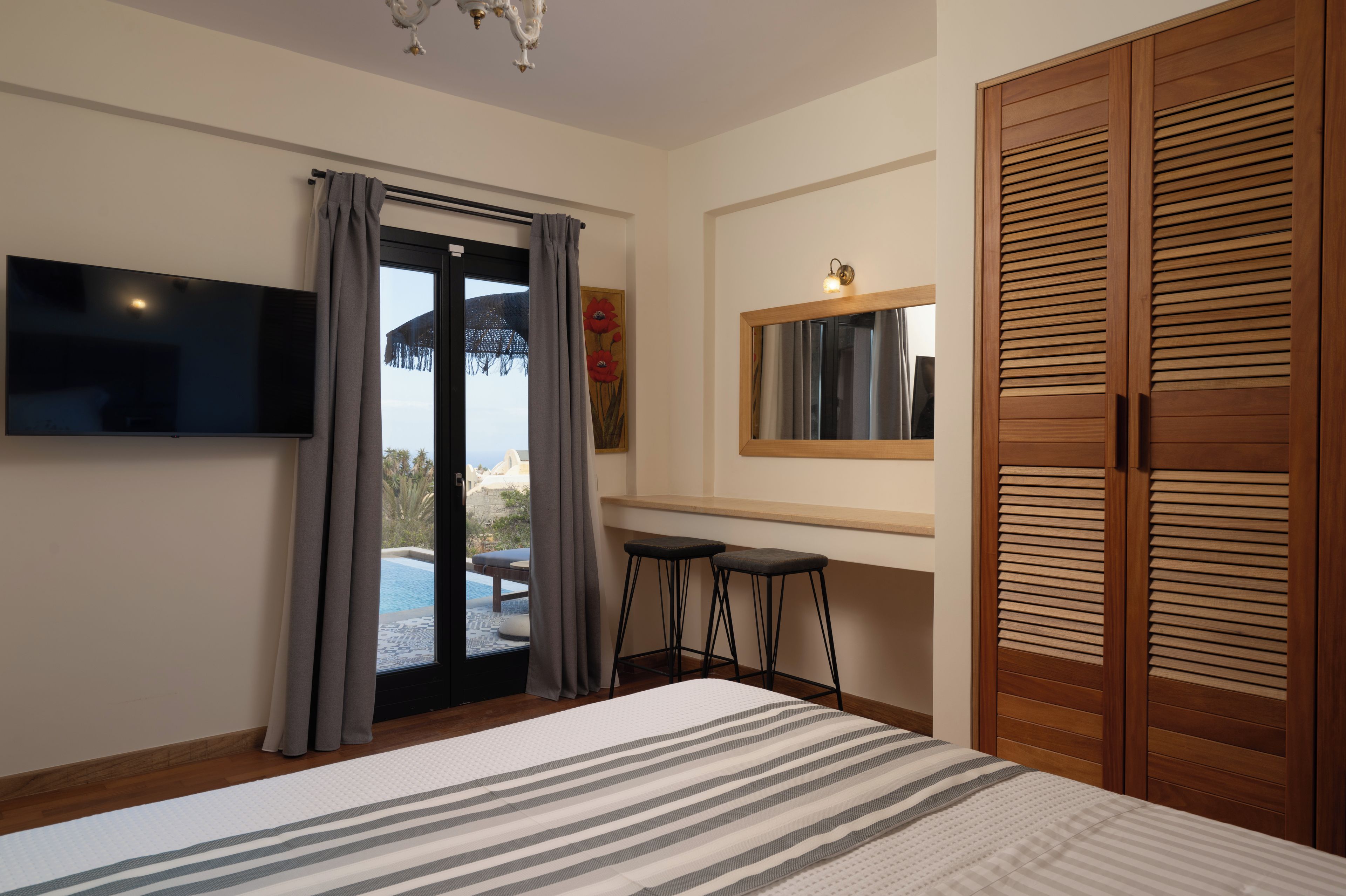 Ein Schlafzimmer mit einem Bett, einem Fernseher, einem Fenster mit Vorhängen, einem Holzschrank und einem kleinen Hocker.
