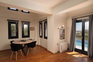 Ein modernes Wohnzimmer mit Holzboden, einem runden Esstisch mit Stühlen, einer integrierten Klimaanlage und einem großen Schiebeglasfenster mit Blick ins Freie.