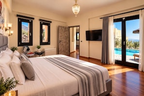 Un dormitorio con una cama grande, televisión, puerta corrediza a una piscina y vistas al exterior.