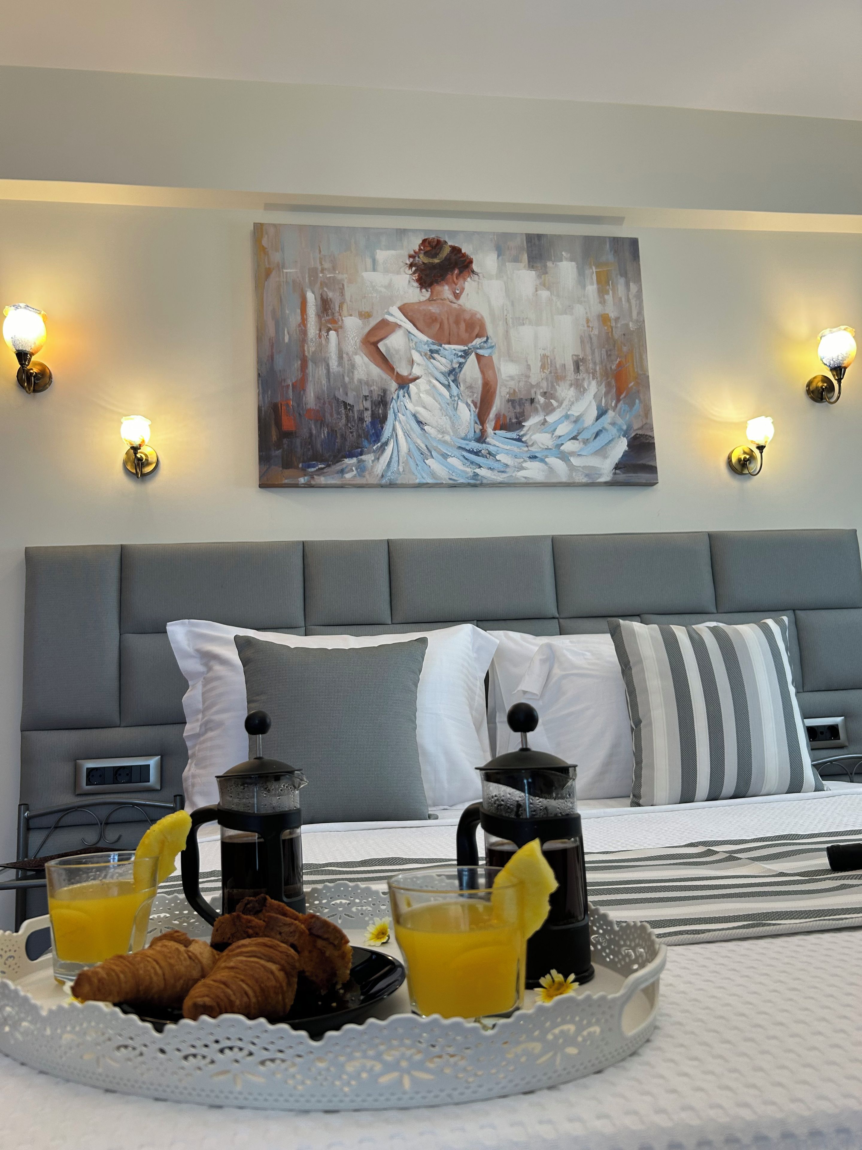 Een hotelkamer met een bed, een schilderij aan de muur en een ontbijttafel met croissants en sinaasappelsap.