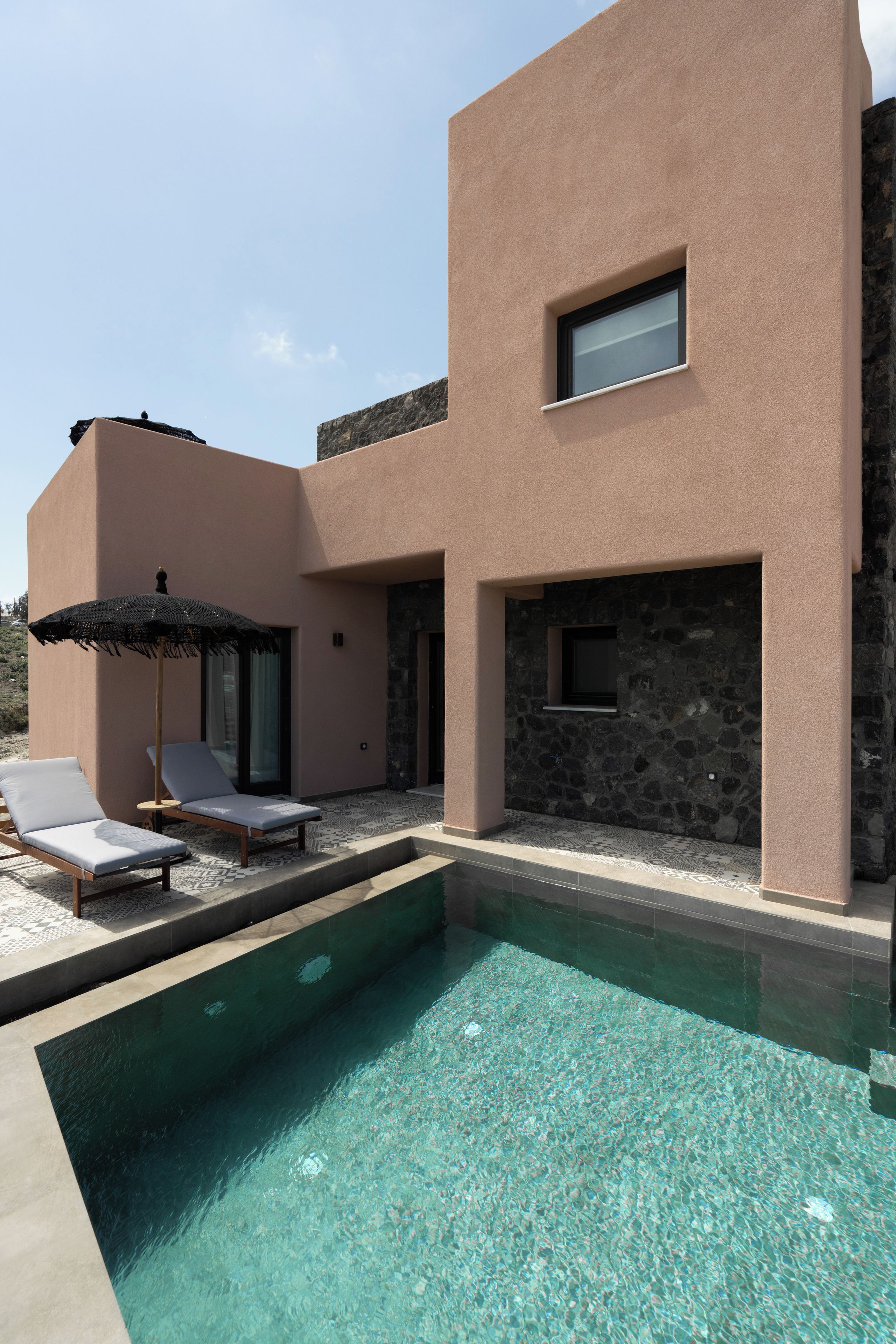 A modern house with a swimming pool, two lounge chairs, and a small patio area.
