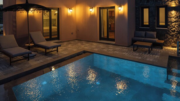 Ein modernes Haus mit Swimmingpool, Liegestühlen und einer Steinmauer.