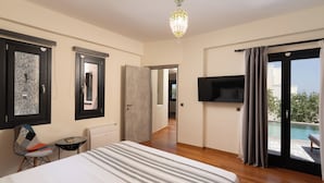 Ein Hotelzimmer mit Bett, Fernseher, Blick auf einen Pool und einer Tür zu einem weiteren Raum.