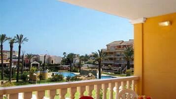 Un balcón con vistas a una piscina y palmeras, una mesa con una silla, y un edificio al fondo.