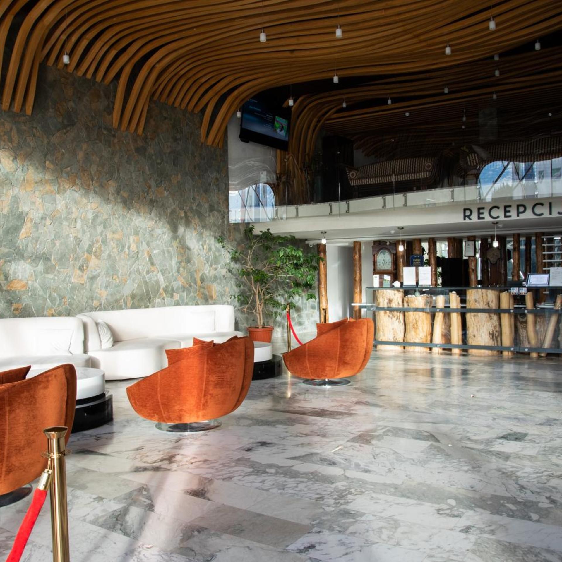 A lobby with a reception desk, a white sofa, and two orange chairs.