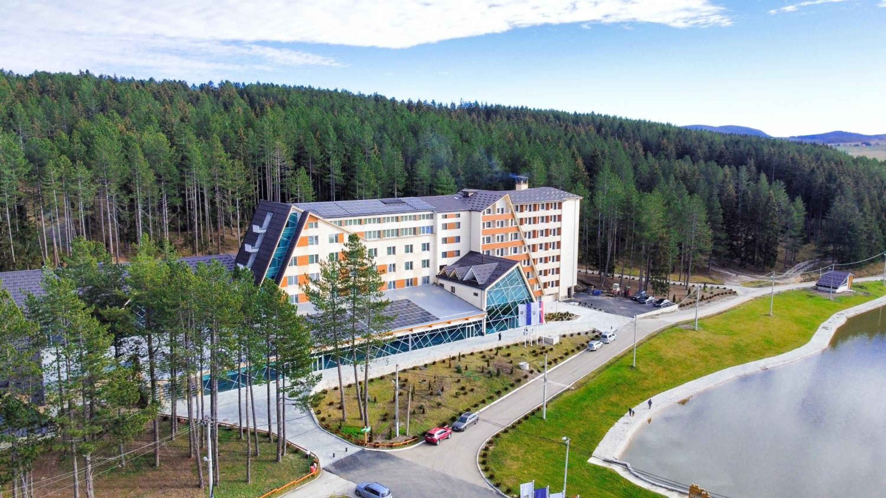 A multi-story hotel with a modern design, surrounded by a forested area and a body of water.