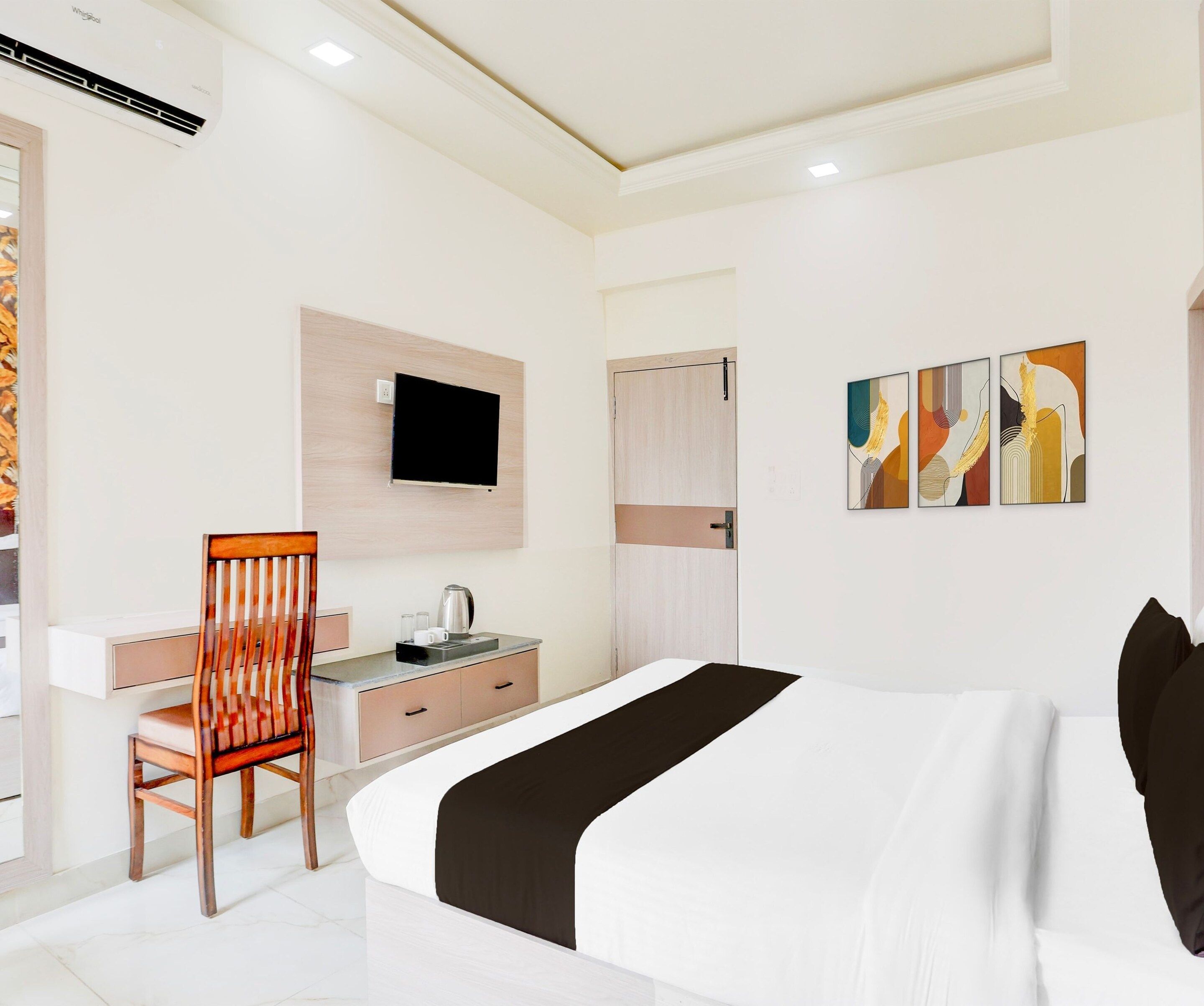 Una habitación de hotel con una cama, un escritorio, una silla, un televisor y obras de arte en la pared.