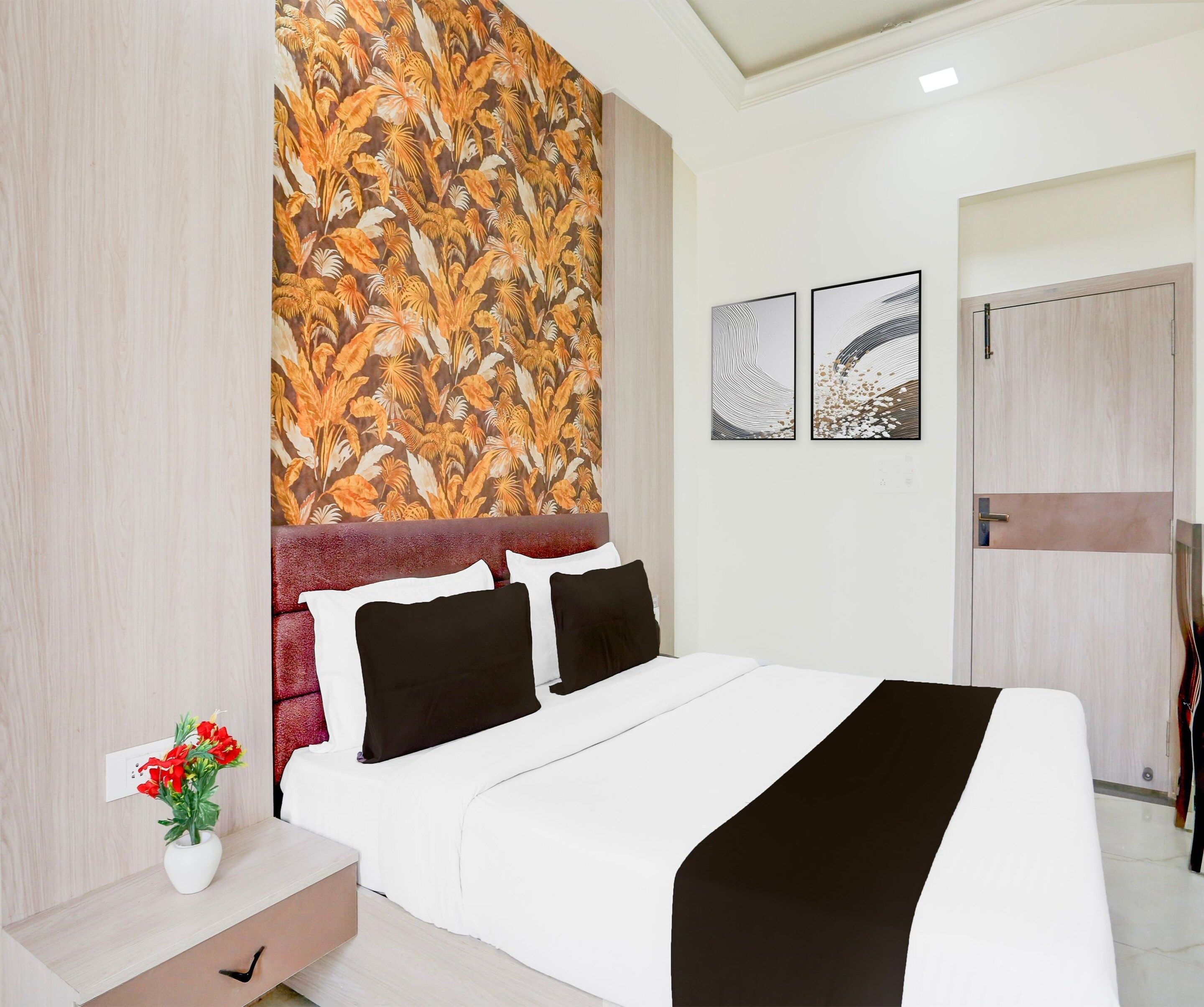 A hotel room with a bed, a nightstand, a wall with a tropical leaf pattern, and two framed artworks on the wall.