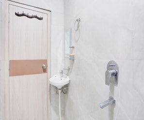 Une salle de bain avec une porte en bois, un lavabo blanc, un miroir et une douche.