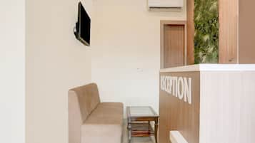 Un área de recepción con un sofá, una mesita y un televisor montado en la pared.