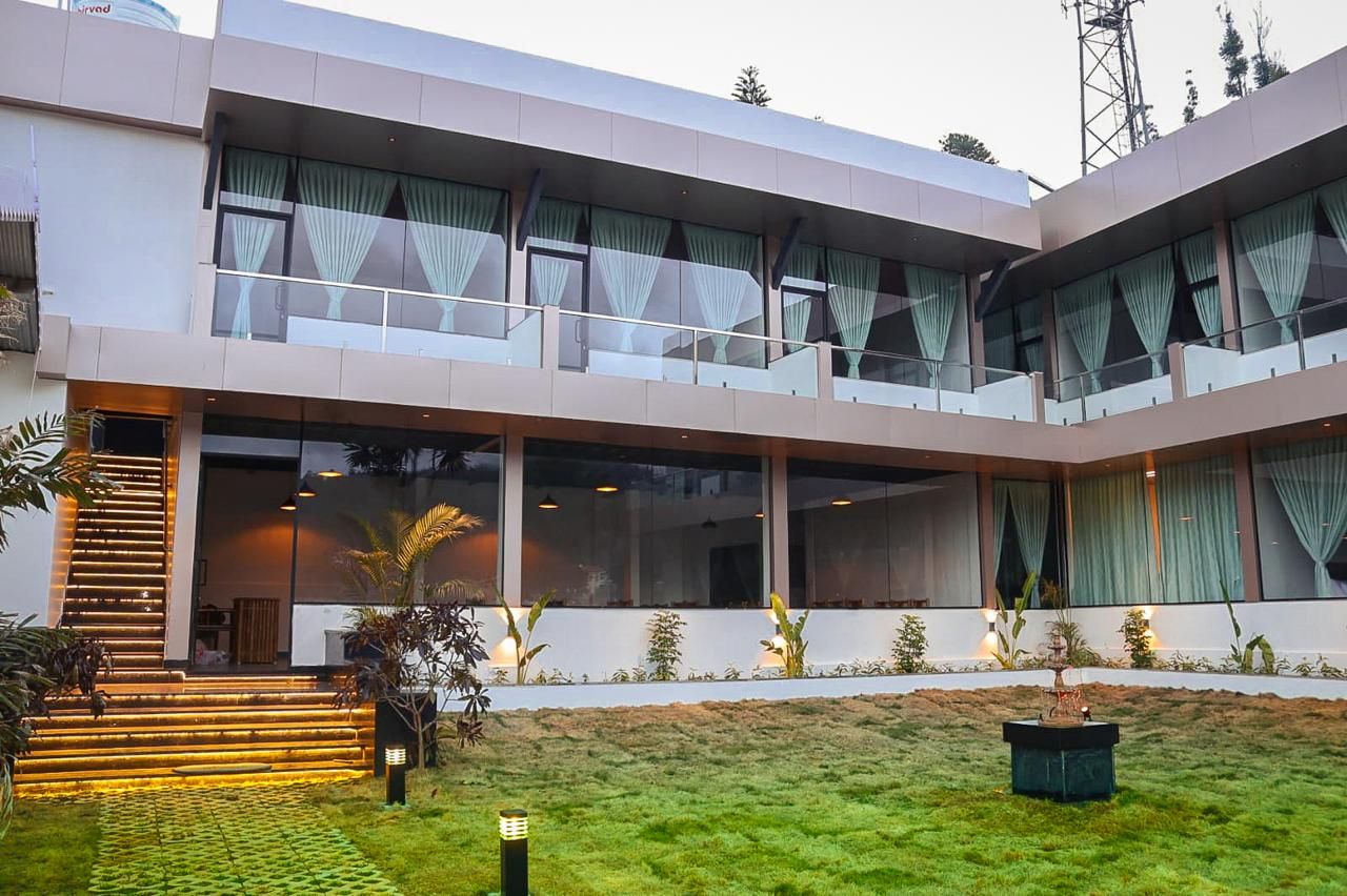 A modern multi-story building with large windows, a staircase, and a well-maintained lawn.