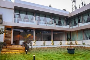 A modern multi-story building with large windows, a staircase, and a well-maintained lawn. - Vintage Inglenook LLP (Ooty)