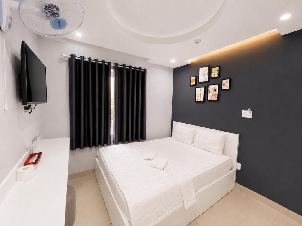 A modern bedroom with a bed, a bedside table, a flat-screen TV, a window with curtains, and a wall with framed pictures.