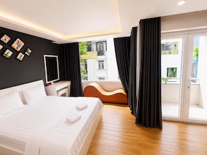 Quarto de hotel com cama, escrivaninha, um violão e vista para o exterior.