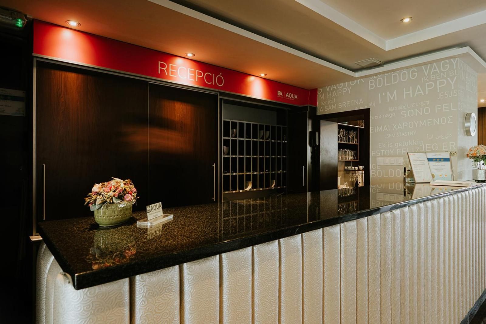 A reception area with a reception desk, a red sign above it, and a wall with various text and logos.