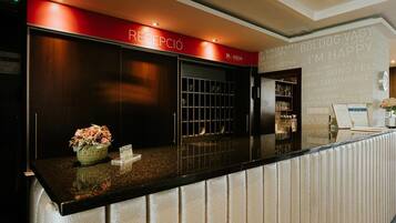 A reception area with a reception desk, a red sign above it, and a wall with various text and logos.