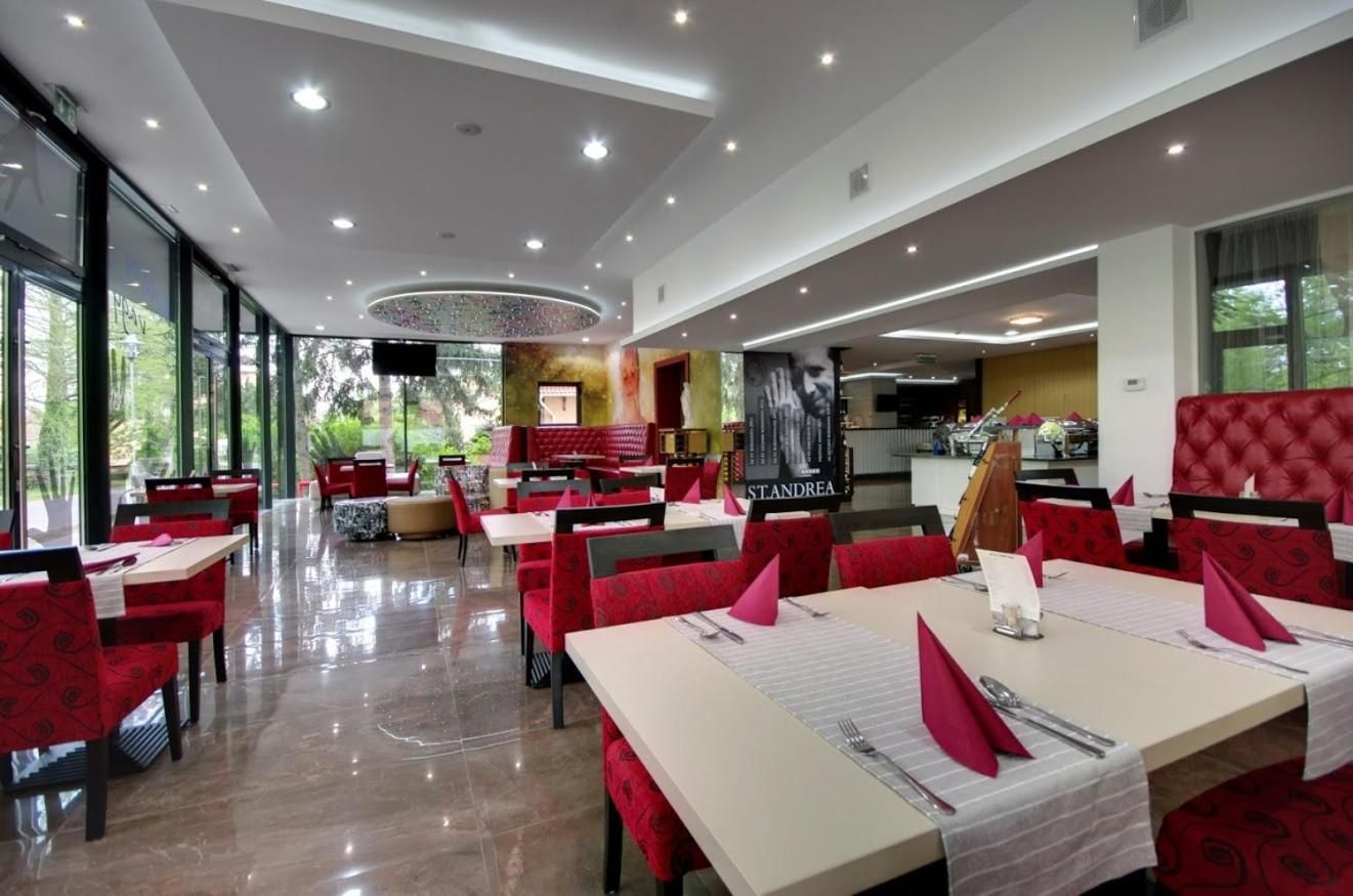 A restaurant with red upholstered chairs and tables, a modern ceiling design, and large windows allowing natural light.