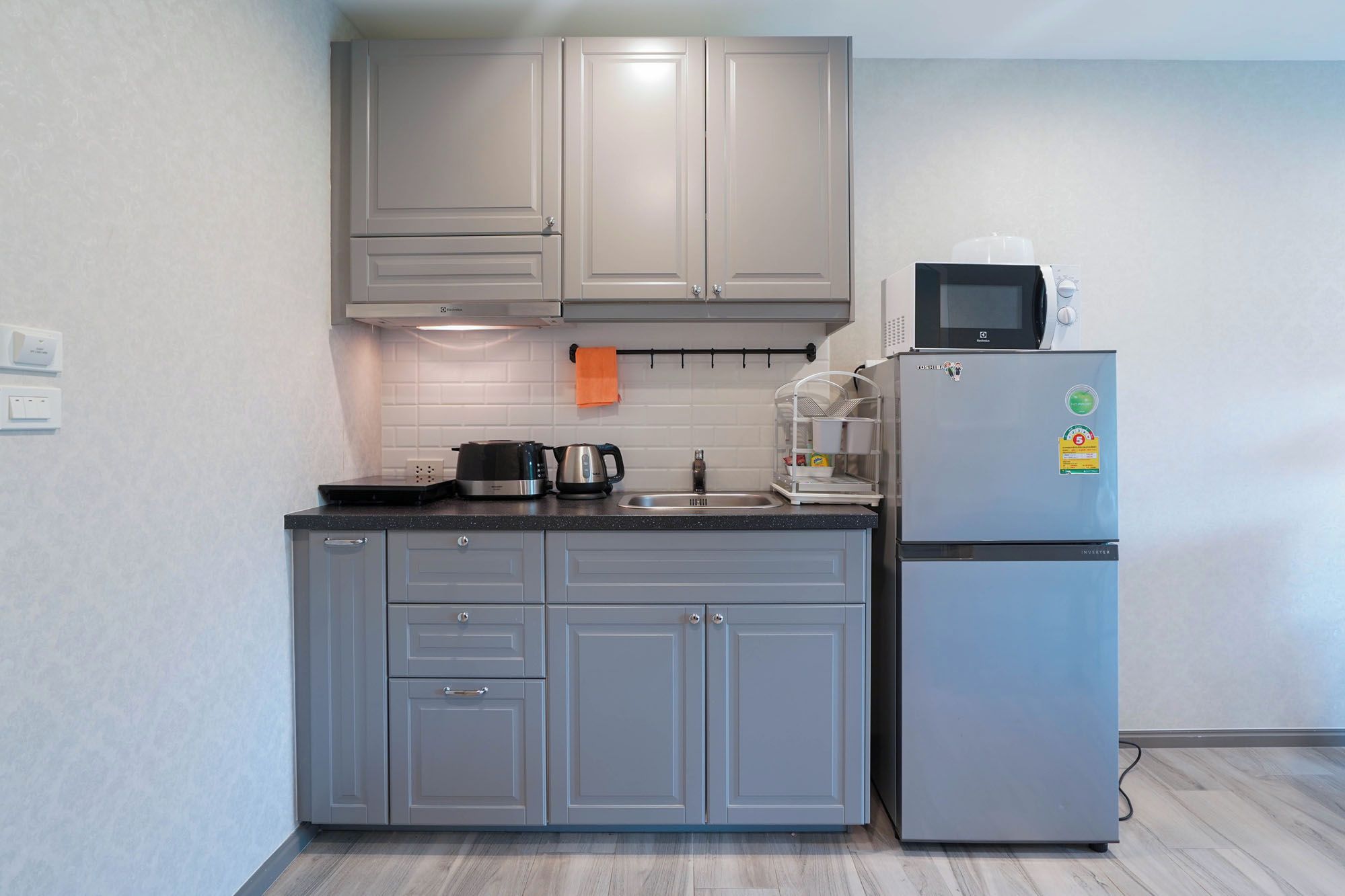 Una cocina compacta con armarios grises, un lavamanos de acero inoxidable, un microondas y un refrigerador.