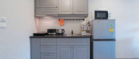 Una cocina compacta con armarios grises, un lavamanos de acero inoxidable, un microondas y un refrigerador.