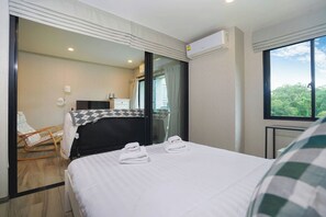A hotel room with a bed, a chair, a desk, and a window with a view of greenery. - Apartment Near Nai Yang Beach - Pool View 1BR Condo with Gym & Fast Wi-Fi - B403 (Tambon Sa Khu)