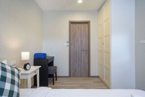 Ein Hotelzimmer mit Bett, Schreibtisch mit Lampe, Stuhl, Kleiderschrank und Tür.
