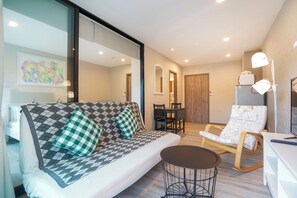A modern living room with a sofa, a small round table, a rocking chair, and a dining table with chairs. - Apartment Near Nai Yang Beach - Pool View 1BR Condo with Gym & Fast Wi-Fi - B403 (Tambon Sa Khu)