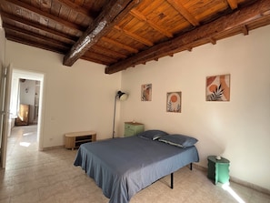 A bedroom with a wooden ceiling, a bed with a blue bedspread, a bedside table, a floor lamp, and two wall-mounted artworks. - Nice downtown apartment (Cavaillon)