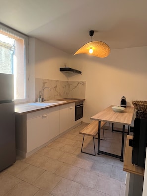 A modern kitchen with a built-in oven, a sink, and a dining area with a table and bench. - Nice downtown apartment (Cavaillon)