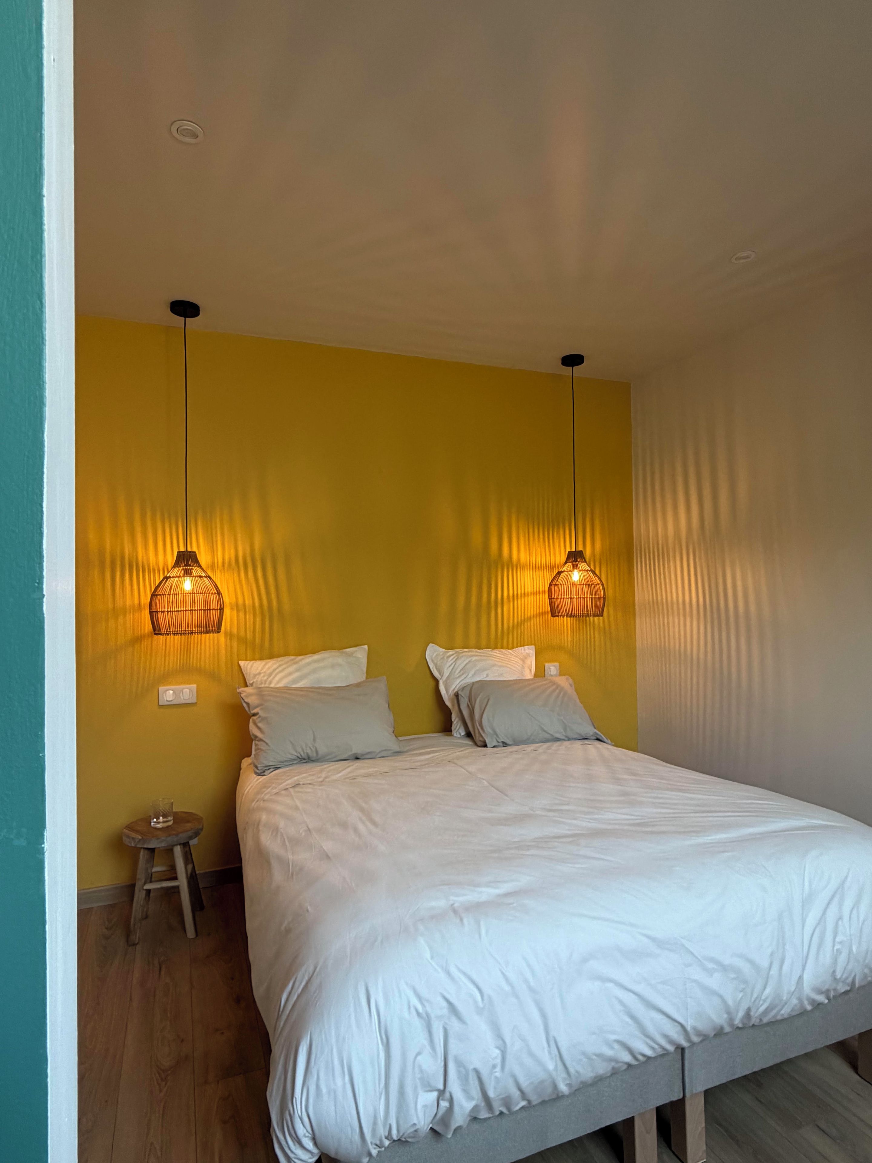 Un dormitorio con una cama, dos lámparas de pared, una mesita de noche y un taburete pequeño.