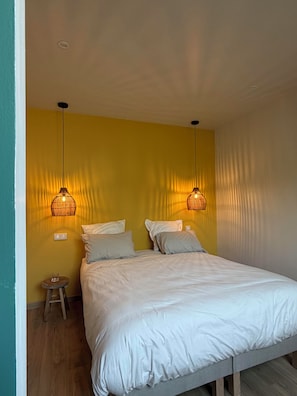 Un dormitorio con una cama, dos lámparas de pared, una mesita de noche y un taburete pequeño.