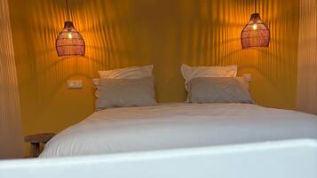 Una cama con ropa de cama blanca, dos lámparas de noche y suelo de madera.