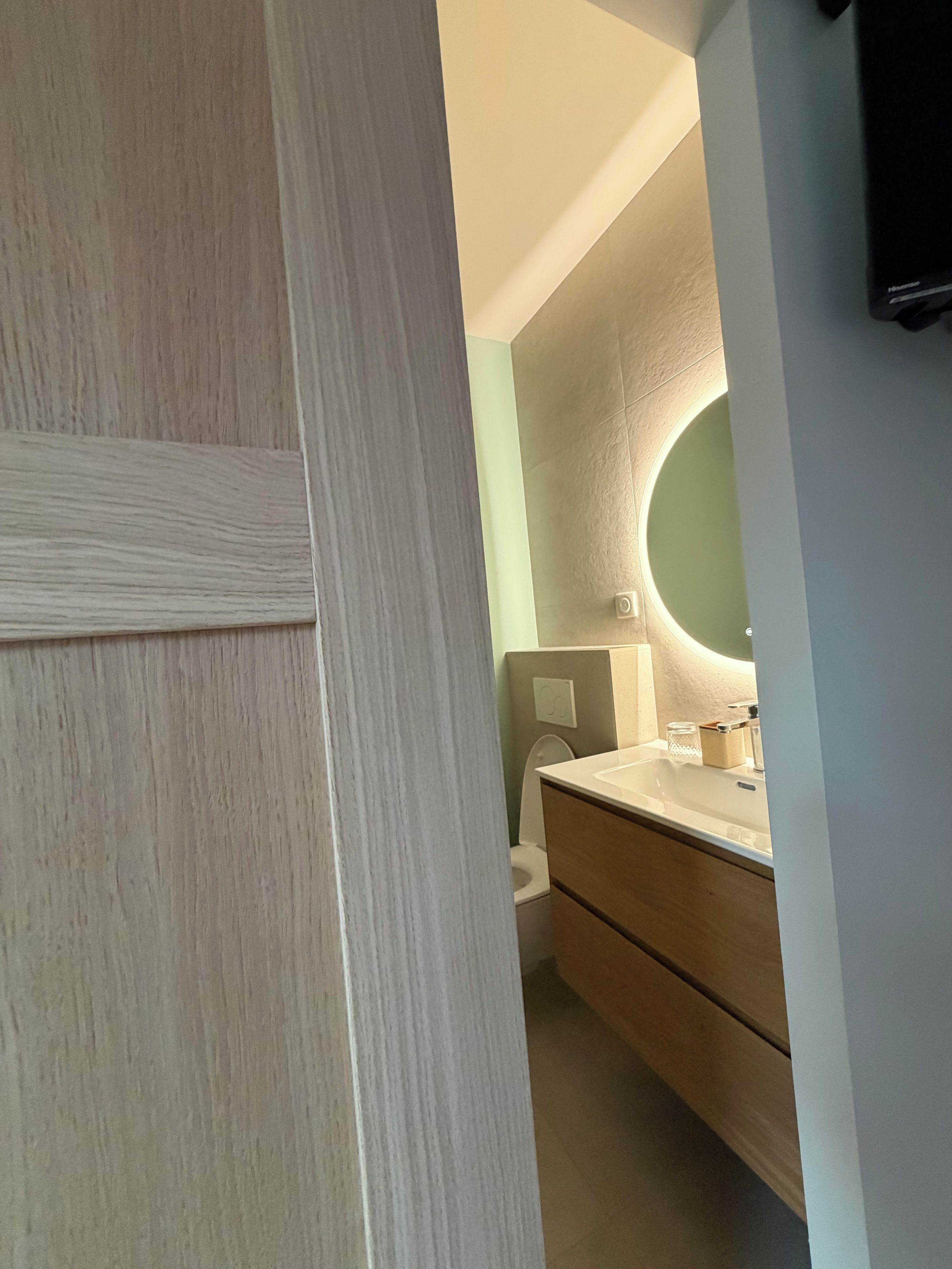 A bathroom with a wooden vanity, a round mirror, and a toilet.