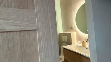 A bathroom with a wooden vanity, a round mirror, and a toilet.