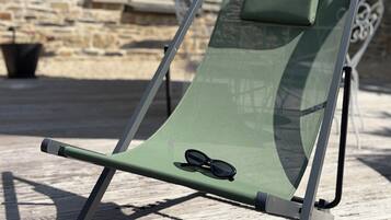 A green lounge chair with a pair of sunglasses on it, positioned on a wooden deck with a stone wall in the background.
