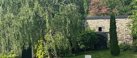 A garden with a stone wall, two white chairs, and a variety of greenery.