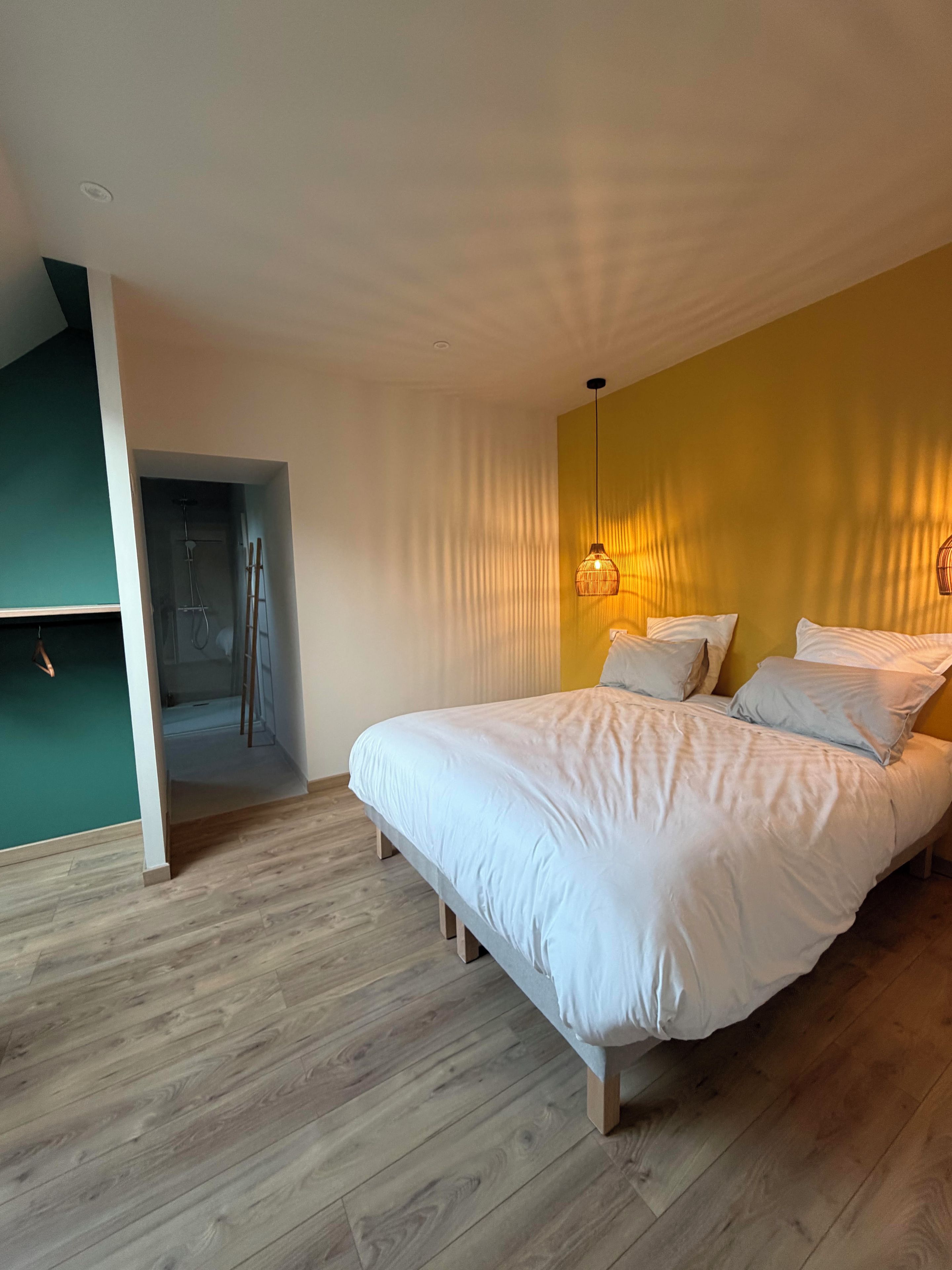 A bedroom with a bed, a hanging light fixture, and a wooden floor.
